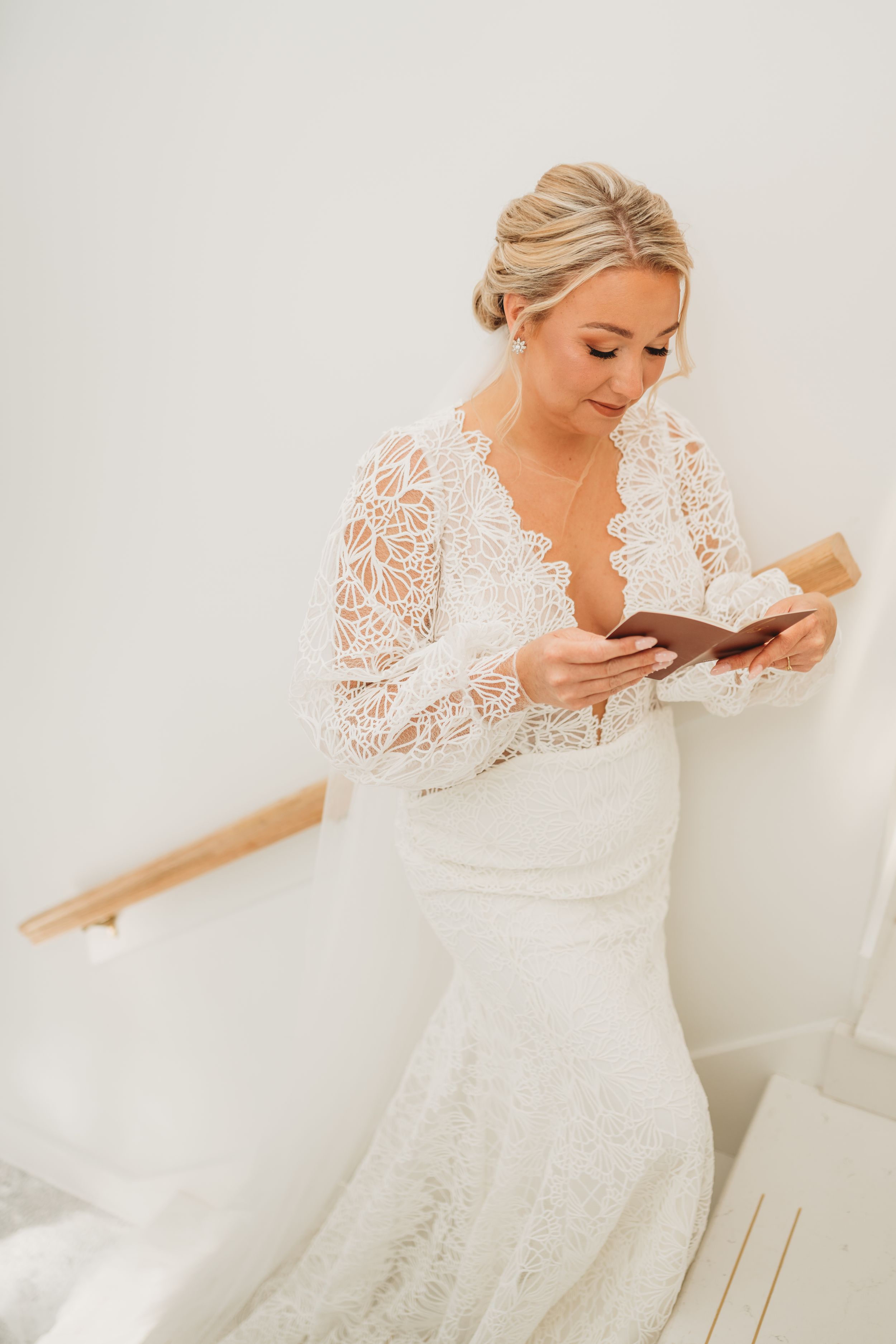 Bride in lace wedding dress reading a letter while getting ready.