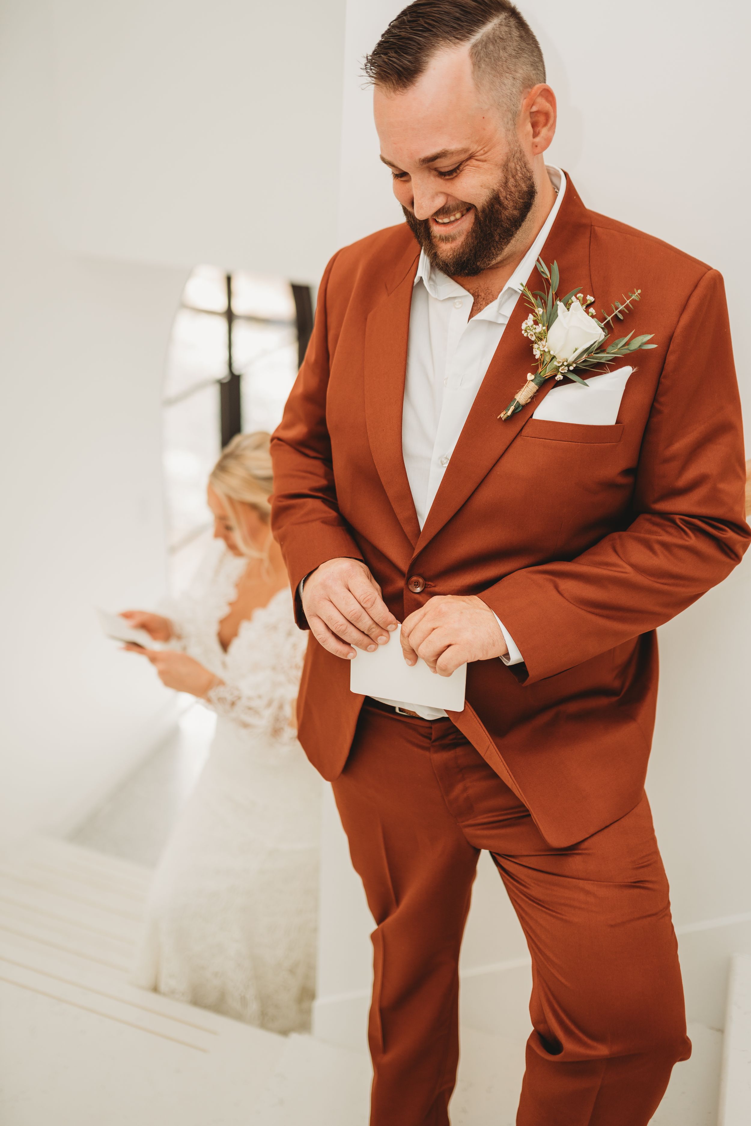 Groom in rust-colored suit smiling while getting ready for wedding ceremony.
