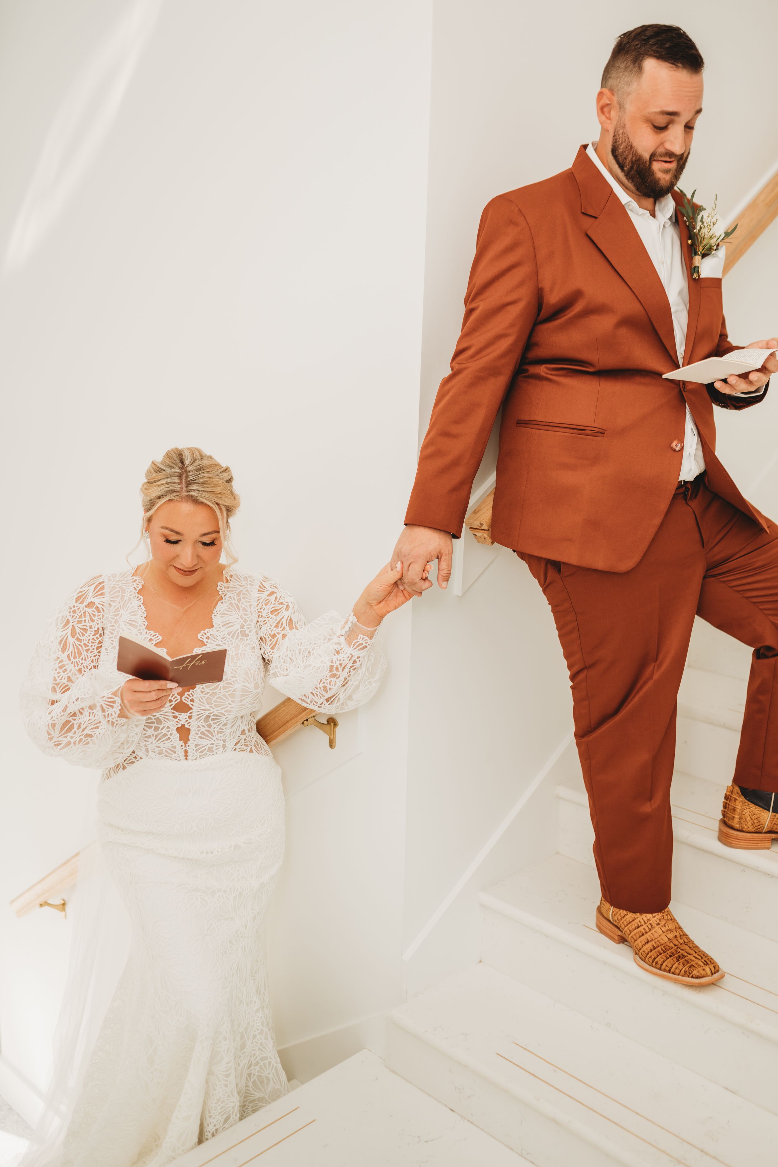 Bride and groom reading private letters on elegant white staircase.