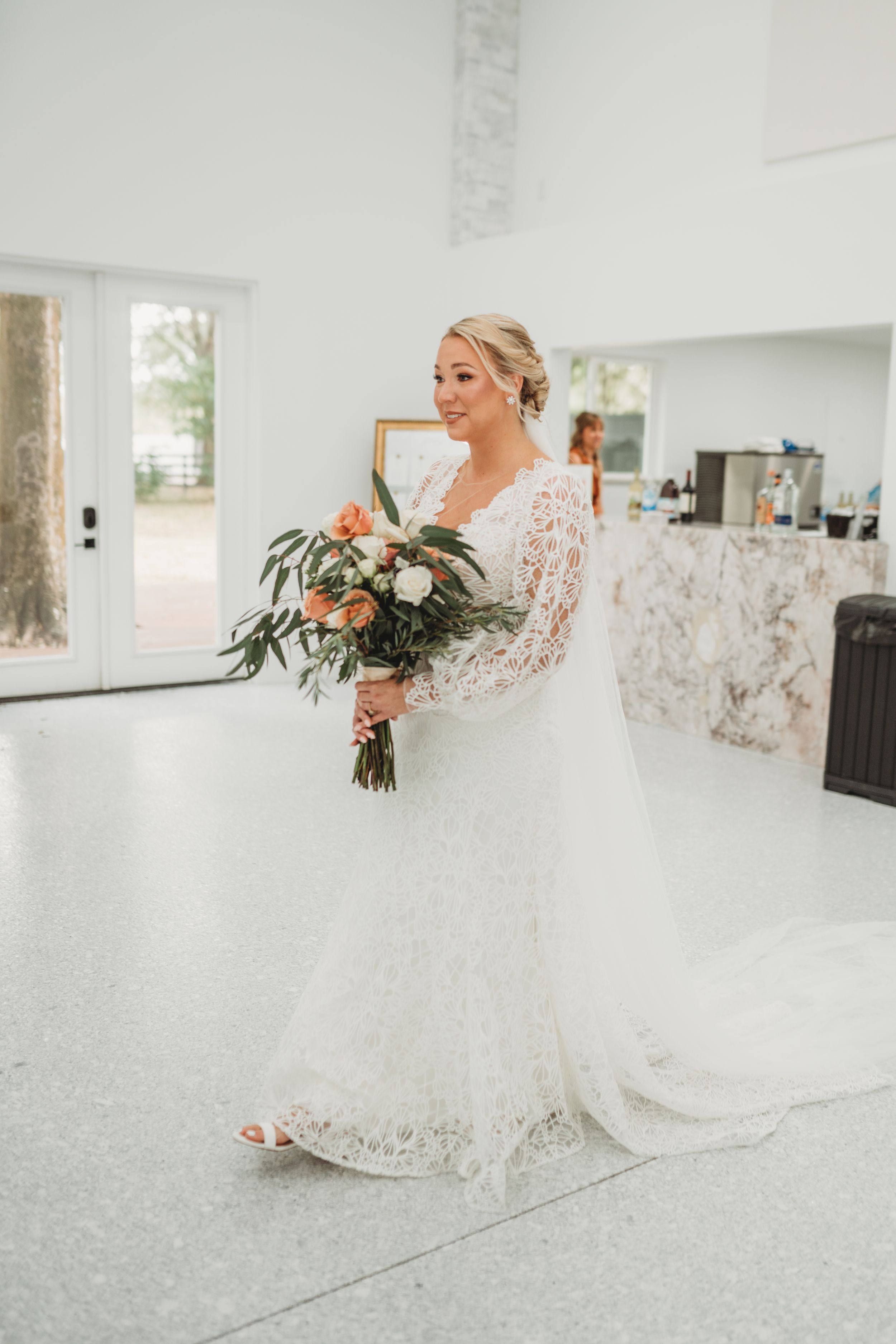Bride in lace wedding dress holding peach and white floral bouquet.
