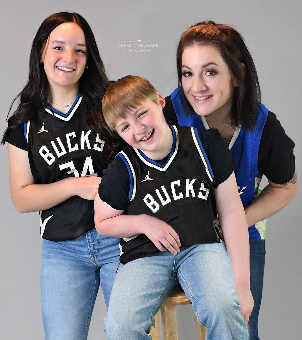 Three enthusiastic Milwaukee Bucks basketball fans wearing black team jerseys pose together for a casual group photo.