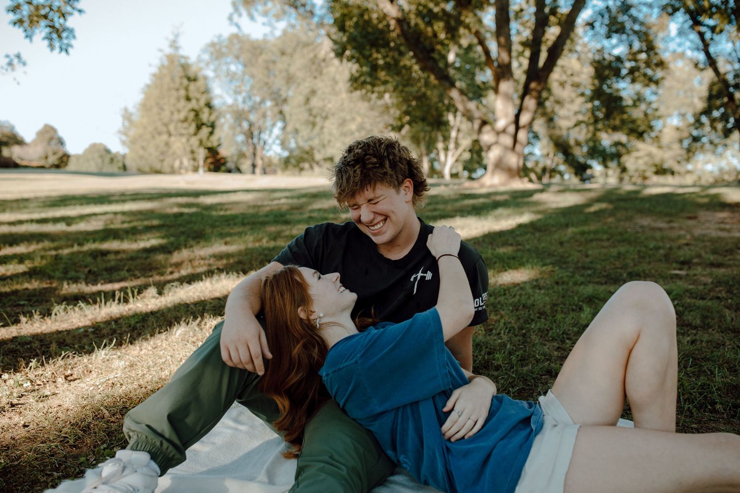 A couple lies in the grass together laughing during a sunny outdoor photo session.