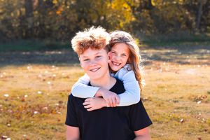 Two people embrace and smile while standing in a golden autumn field during sunset.