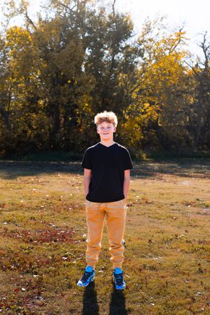Person standing in autumn field wearing black shirt, khaki pants and bright blue shoes as golden leaves fall from trees.