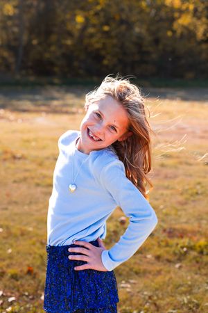 Person in white sweater and blue skirt dances joyfully in autumn field at sunset.