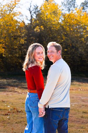 A couple in matching denim and autumn colors share a romantic moment in a field with golden fall foliage.