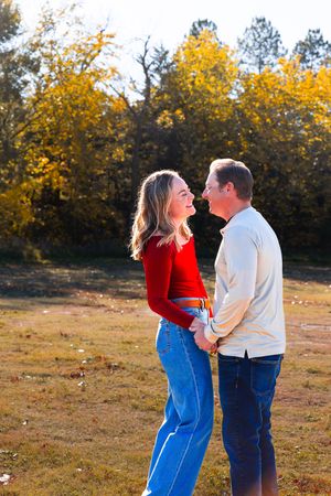 A couple in matching denim and autumn colors share a romantic moment in a field with golden fall foliage in the background.