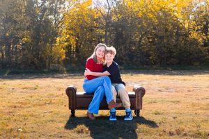 Couple sharing tender moments on brown couch in autumn field during golden hour photoshoot.