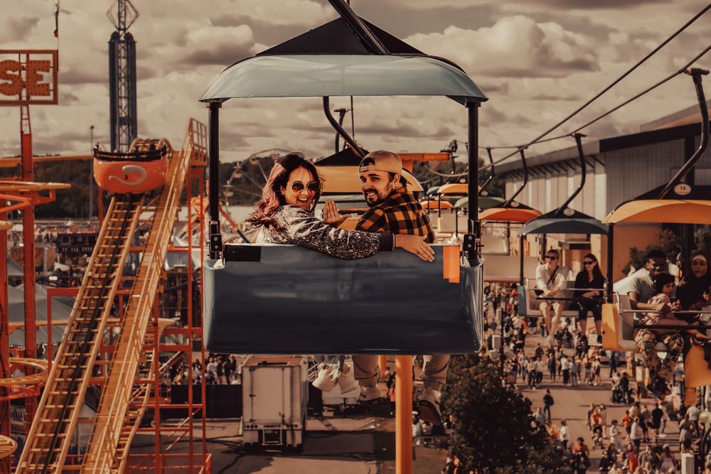 Crowded amusement park with ski lift chairs silhouetted against dramatic cloudy sky.