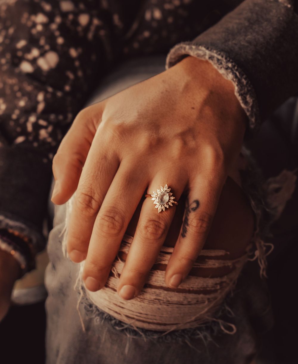 Close-up of a delicate vintage-style ring with crystal details worn on a hand against lace fabric.