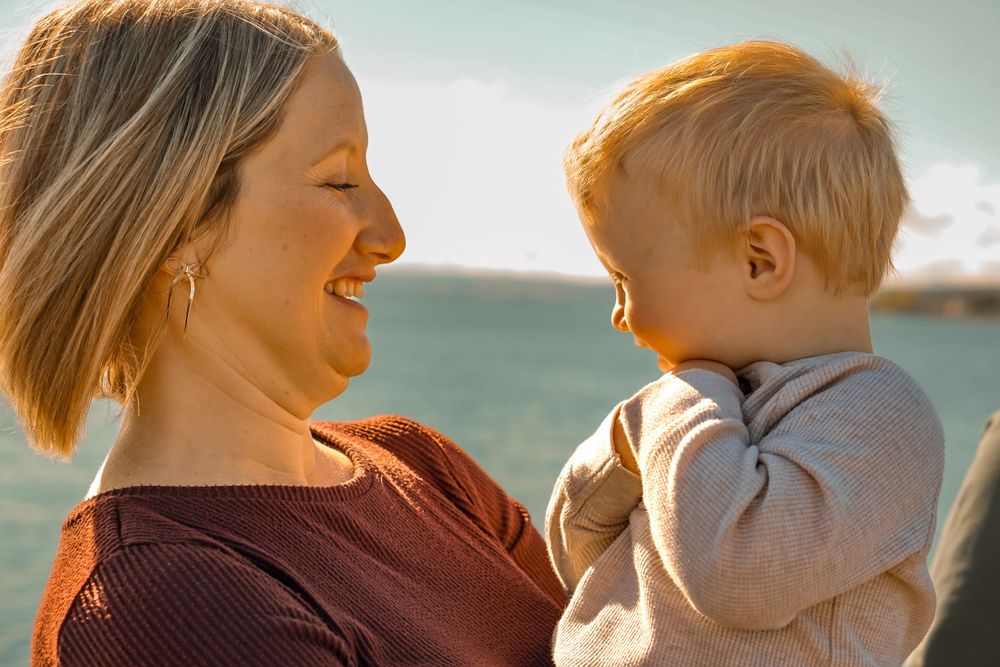 Parent and child sharing joyful moment together against sunny ocean backdrop.