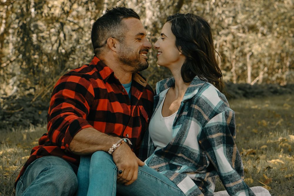 Couple wearing coordinating plaid shirts sharing romantic moment outdoors in autumnal setting.