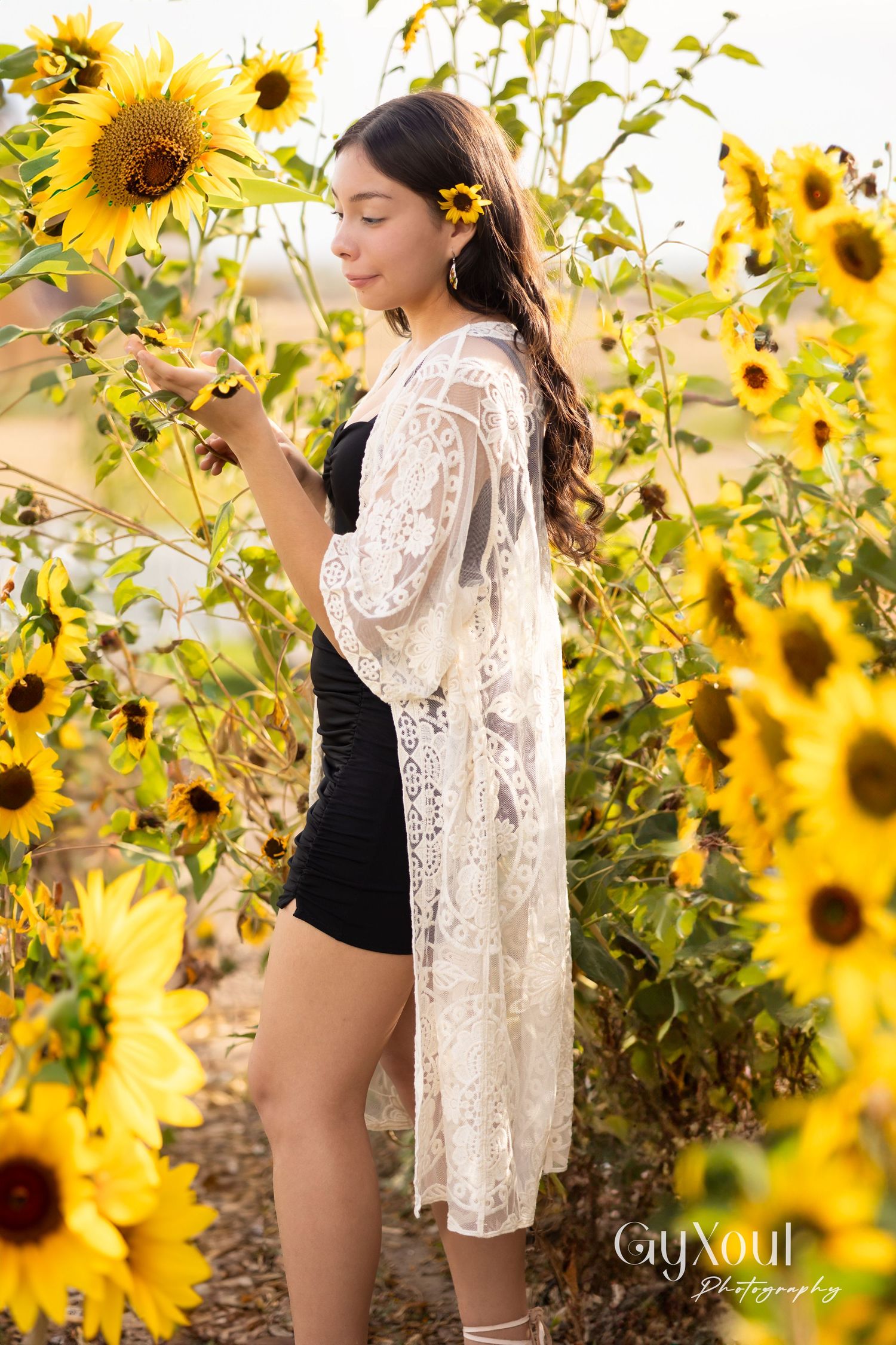 White lace dress contrasts with black outfit in vibrant sunflower field.