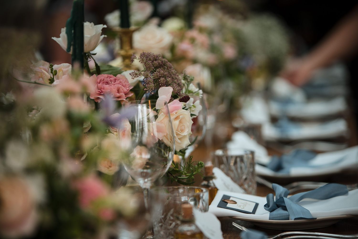 Elegant table setting at wedding reception with soft pink floral centerpieces and blue place settings.