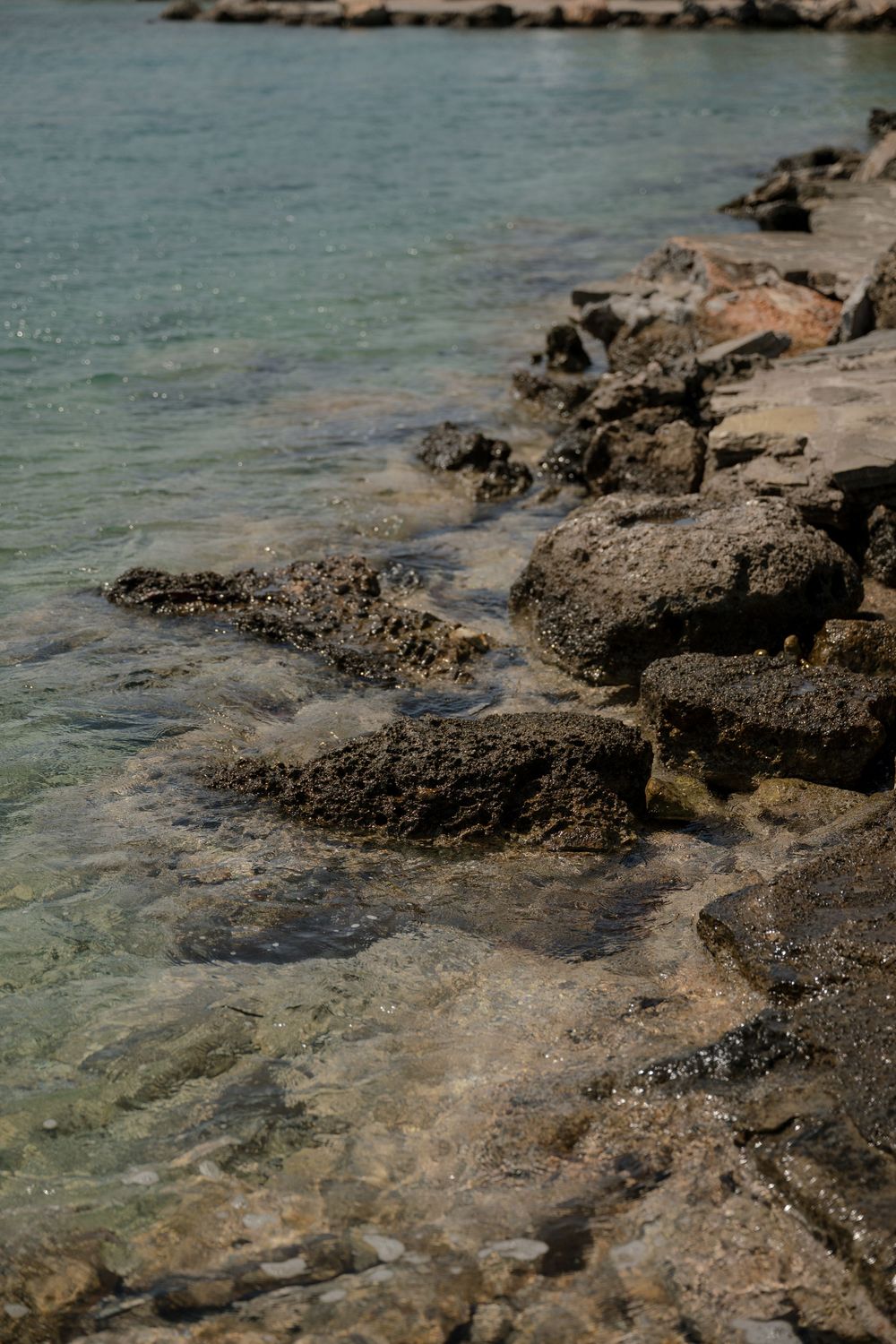 Rocky coastline with turquoise water lapping against weathered stones in shallow Mediterranean waters.