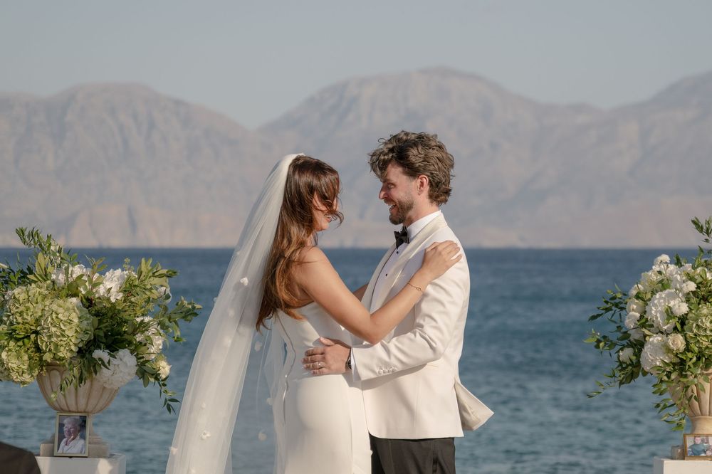 A couple shares an intimate moment at their outdoor wedding ceremony by the ocean with mountain views and floral arrangements.
