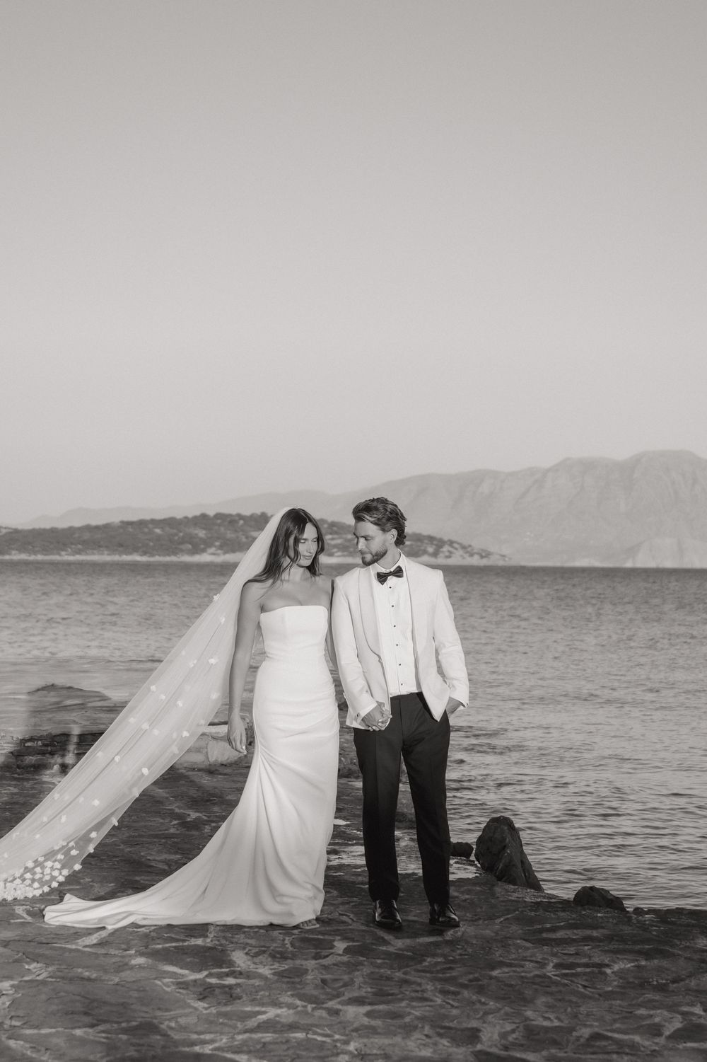 Black and white photos of a couple in wedding attire posing romantically by the ocean at sunset.