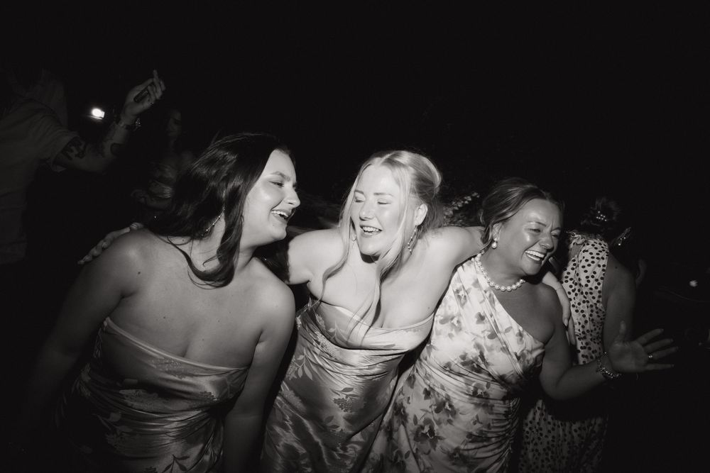 Wedding party guests dancing and laughing together in a dark reception venue.