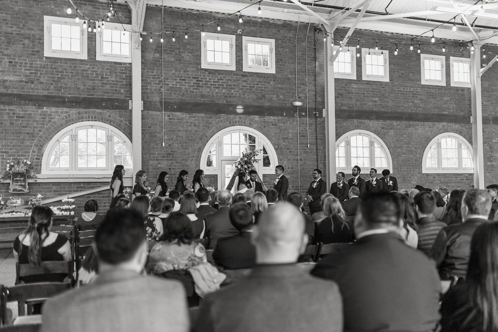 Large crowd seated in rows inside a historic building with arched windows during a wedding ceremony at BRICK Liberty Station