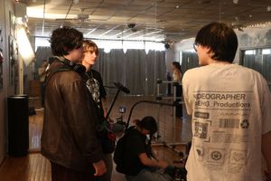 Film crew members work behind the scenes in a dimly lit studio hallway setting.