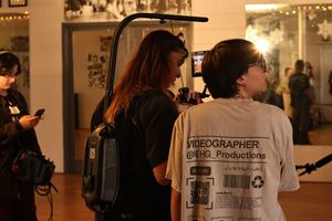 Photographers in white t-shirts work at an indoor event space with gallery lighting and decorative elements.
