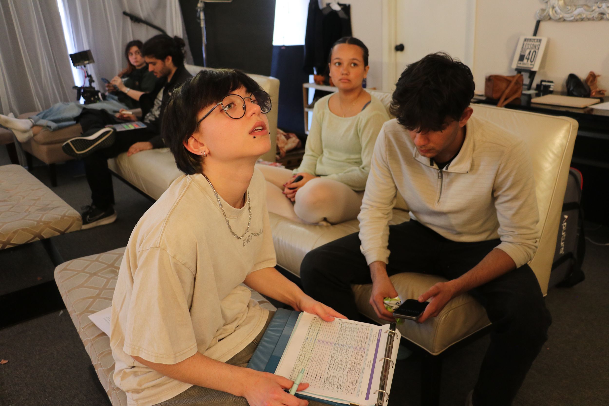 Students study together in a casual living room setting with textbooks and papers spread out on the floor.
