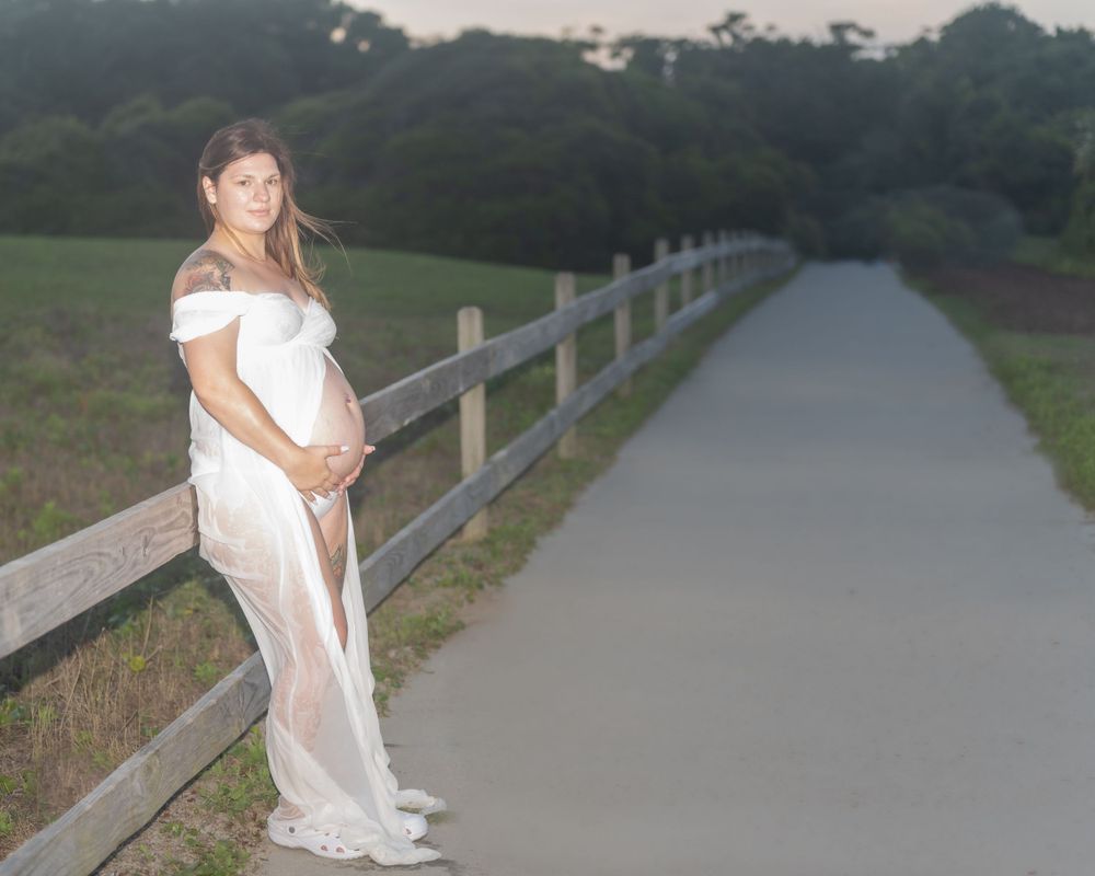 Outdoor maternity photo on path with wooden fence at dusk.