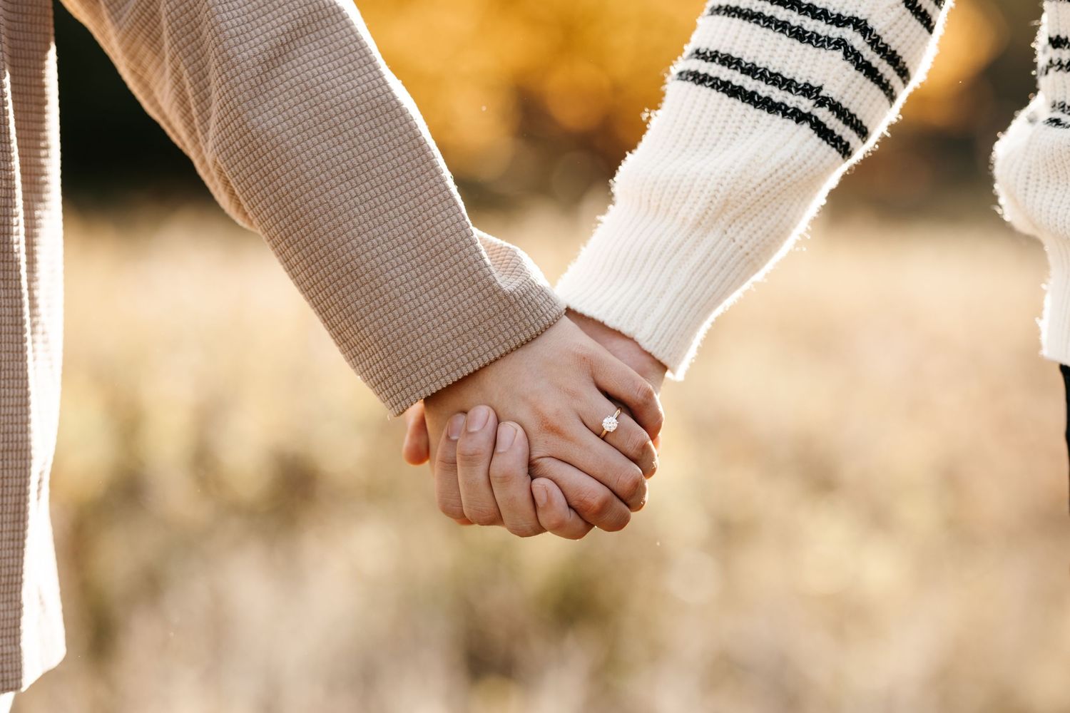 Close-up shot of two people holding hands wearing different textured sleeves.