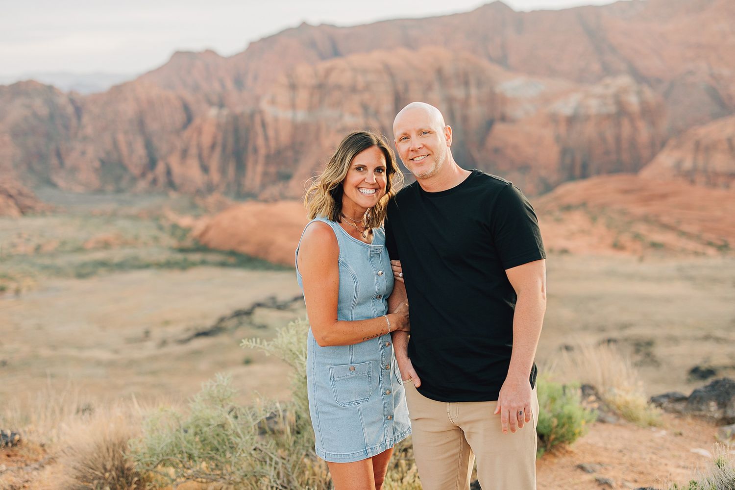 Couple smiling together at red rock canyon landscape during golden hour outdoor engagement photo.