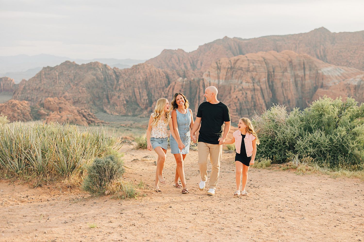 Happy family strolling together on sandy desert path with red rock canyon mountains behind them.
