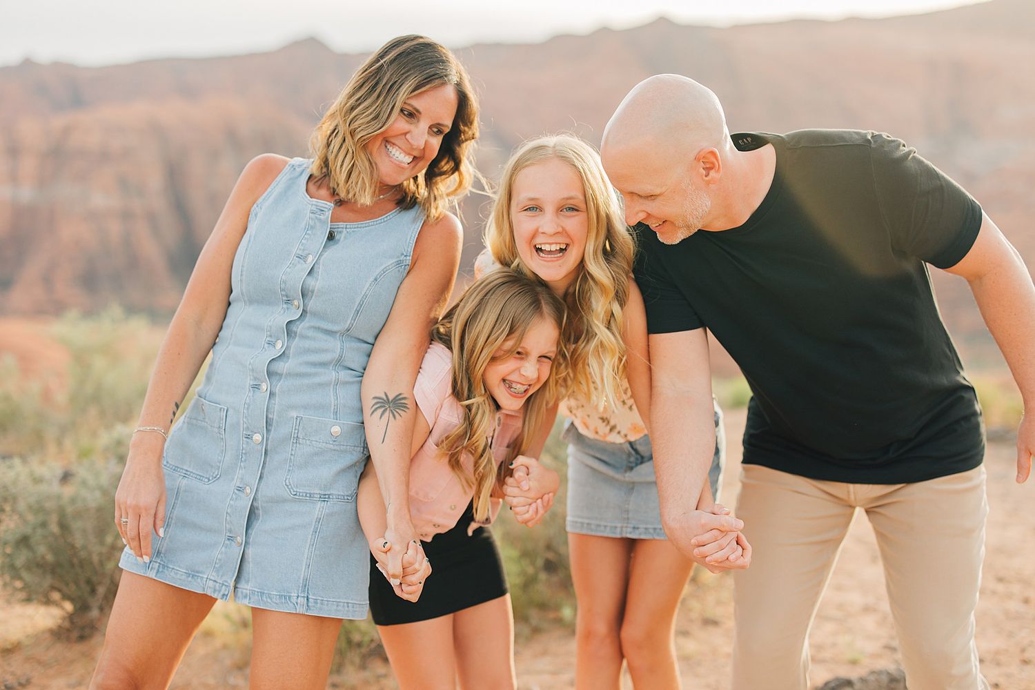 Happy family of four laughing together outdoors with red rock canyon landscape in background.