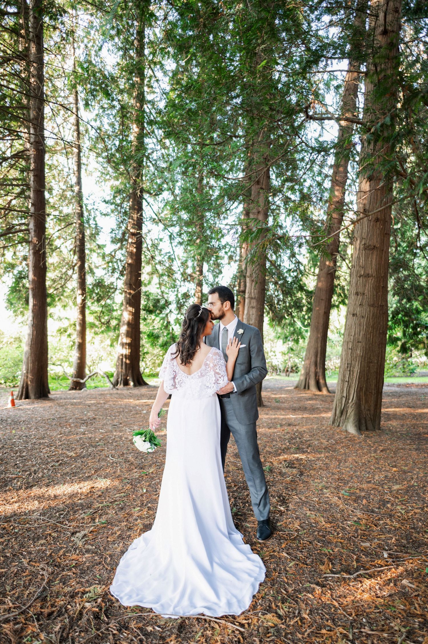 Bride and groom kissing while holding wedding rings in focus at their outdoor wedding ceremony.