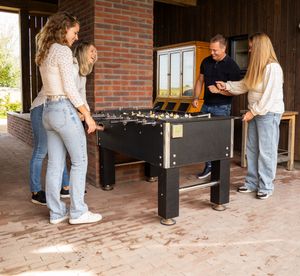 Vier mensen spelen tafelvoetbal in de buitenlucht op een stenen terras vlakbij een stenen muur. familie fotograaf Veluwe