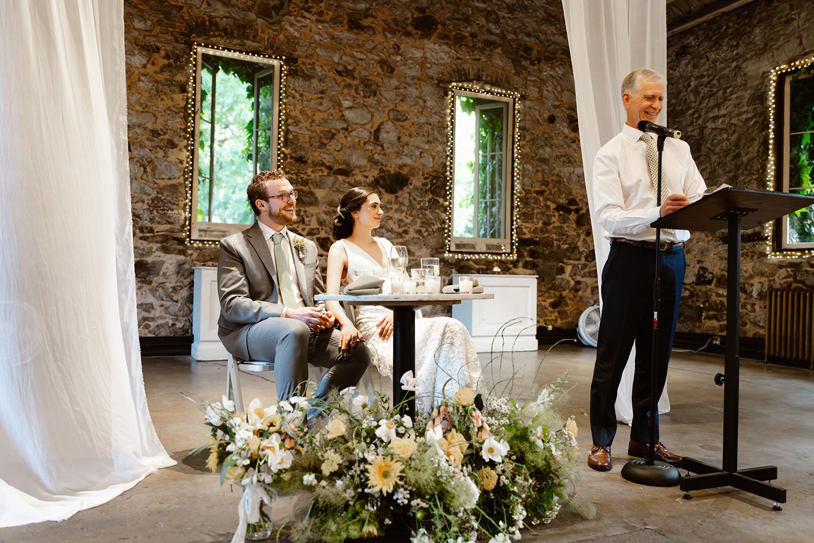 Rustic stone wall venue decorated with white drapes and floral arrangements for an elegant wedding celebration.