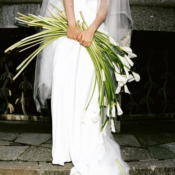 Close-up view of a white calla lily bouquet with long stems being held against a dark background.