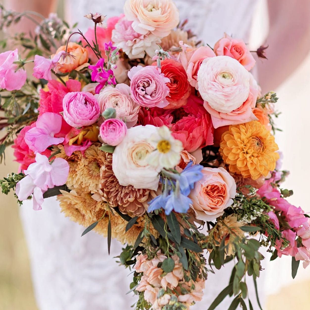 Vibrant wedding bouquet with pink roses, marigolds and mixed flowers arranged in romantic garden style.