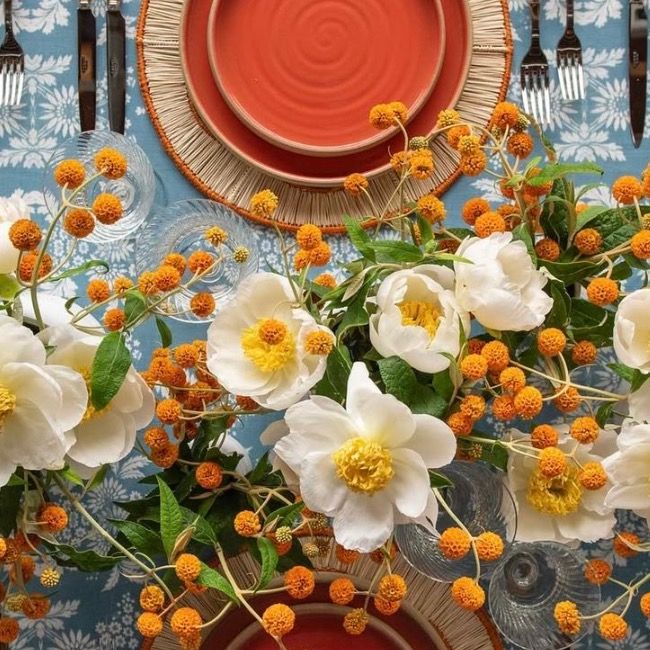 Orange berries and white flowers create a festive table setting with terracotta plates and blue patterned linens.