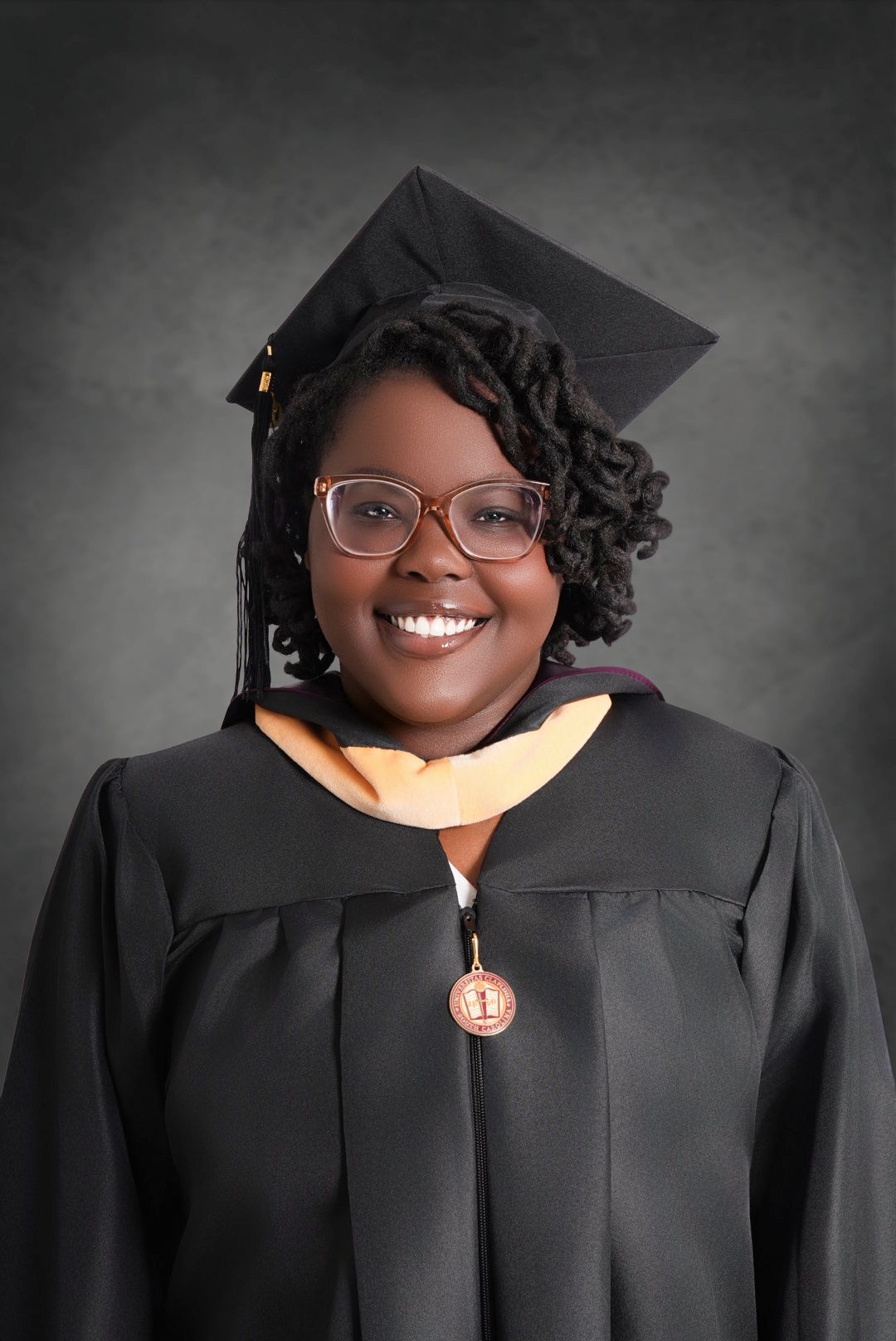 A smiling graduate in a black cap and gown with an orange hood, glasses, and a medal poses for a formal portrait.