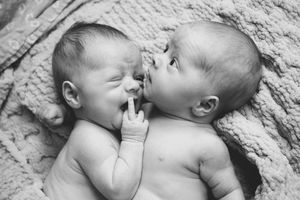 Black and white photo of two newborn twins lying together, one kissing the other on the cheek.