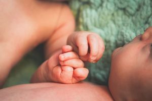 Close-up of a newborn baby's tiny hands and fingers resting peacefully on a green textured blanket.