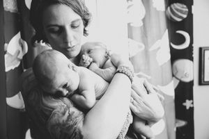 Black and white photo of a mother tenderly cradling two newborn babies in her arms near a window.
