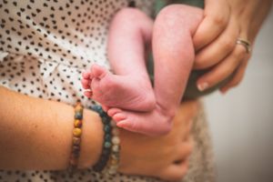 Close-up of tiny newborn baby feet held gently by mother wearing colorful beaded bracelet.