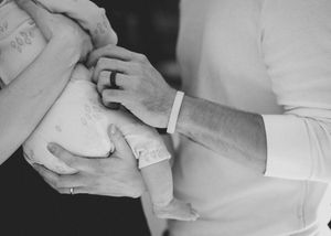Black and white photo of parents holding newborn baby in hospital, wearing ID wristbands after birth.
