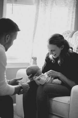 Black and white photo of a smiling mother holding her newborn baby while a man reaches out to touch the infant.