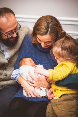 Family of four admiring their newborn baby together, with toddler gently touching the infant.