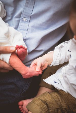 Close-up of father holding newborn baby feet while toddler holds tiny infant hand.