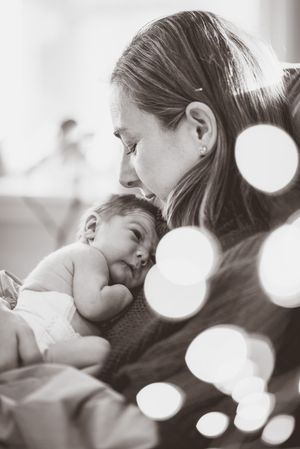 Black and white photo of a mother tenderly holding her sleeping newborn baby close to her chest.