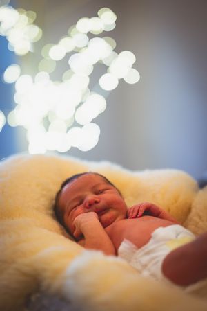 Newborn baby sleeping peacefully on a soft yellow blanket with bokeh lights in the background.