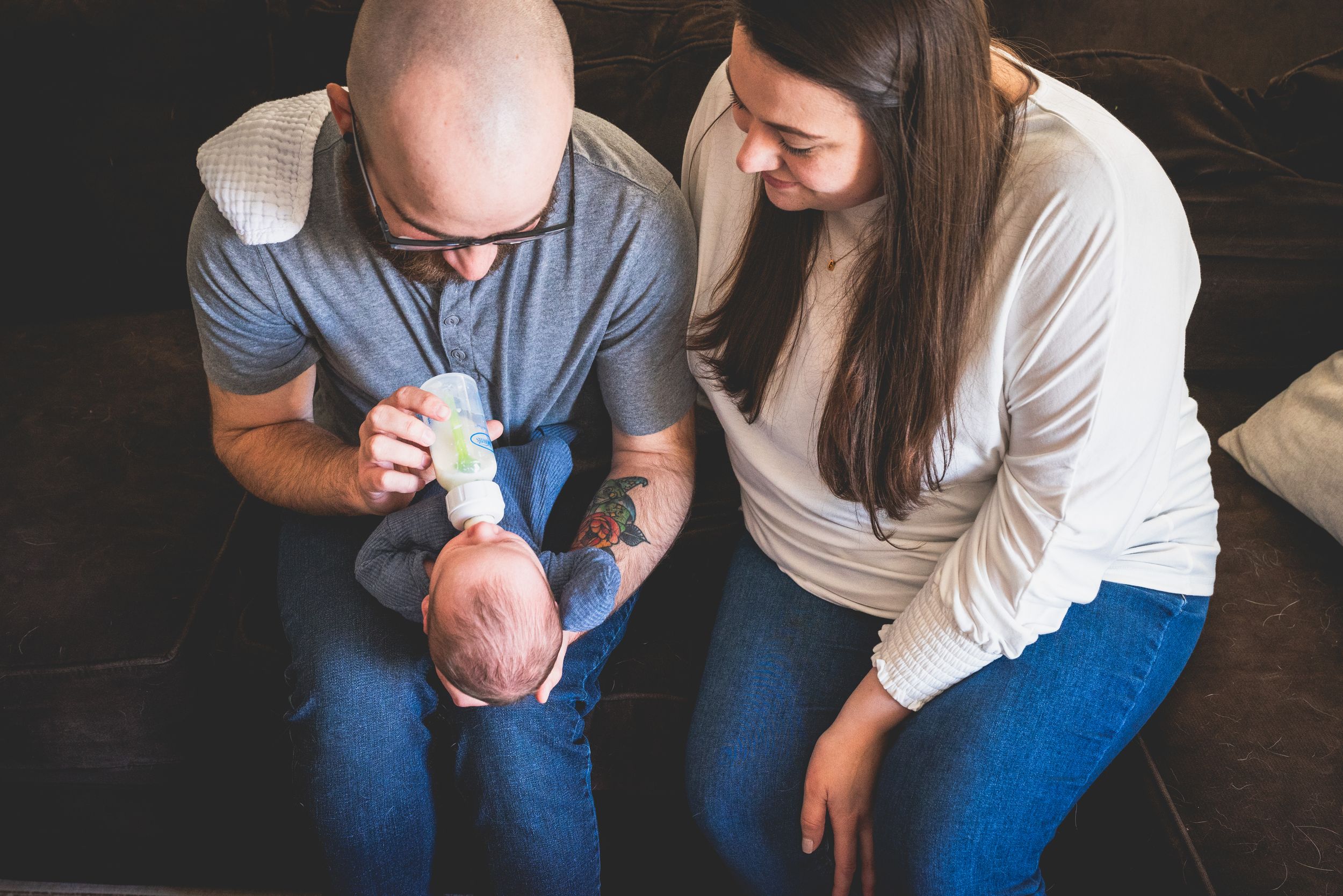 Parents bonding with their newborn baby, father bottle feeding infant while mother watches lovingly.
