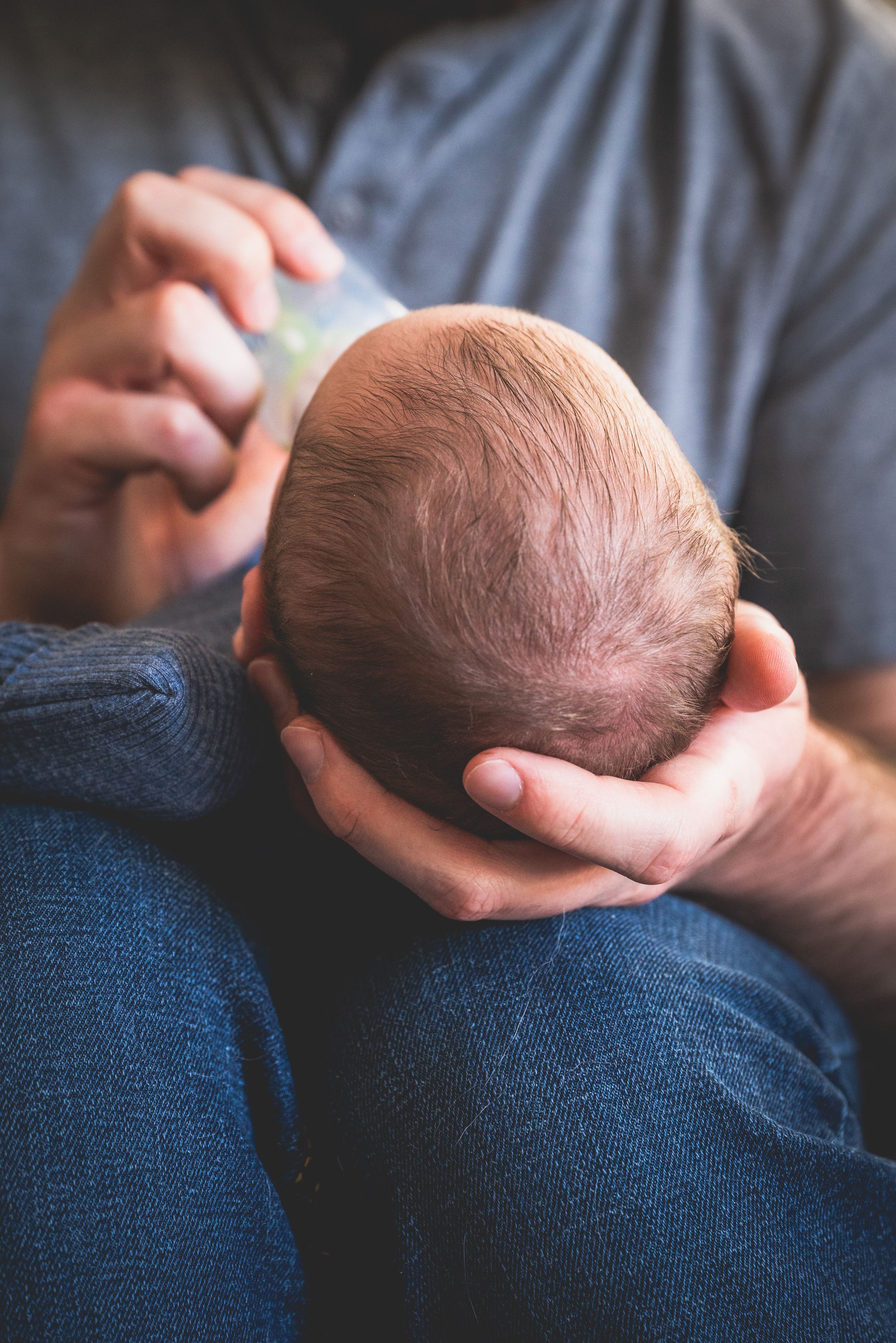 Parent bottle feeding a newborn baby, cradling the infant's head gently in their hand.